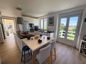 Una cocina moderna con armarios blancos, una isla central y un comedor con sillas a rayas.