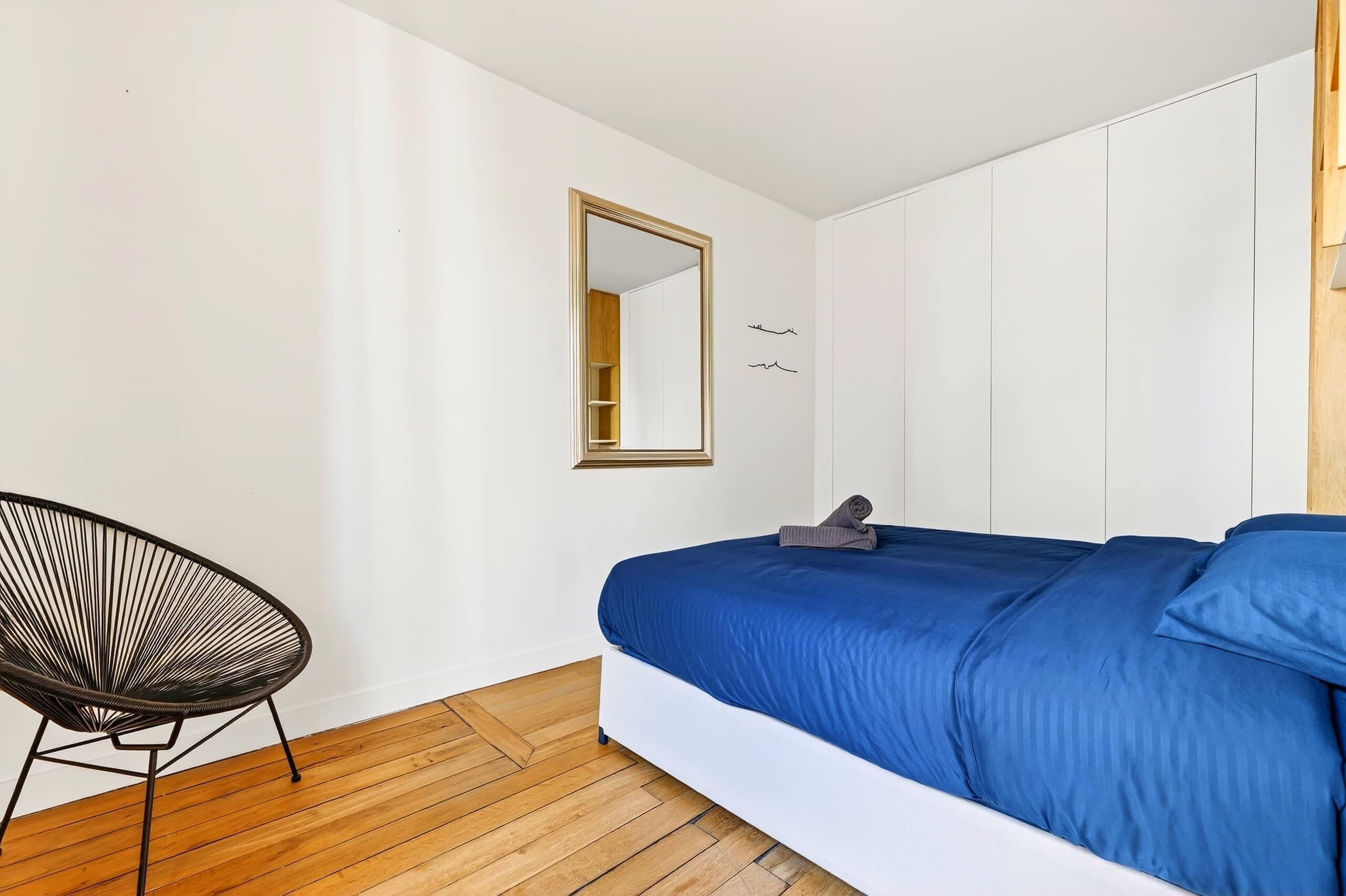 A bedroom with a bed, a chair, a mirror, and a wardrobe.