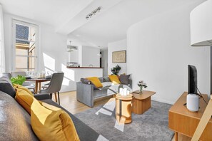 A modern living room with a grey sofa, wooden side tables, and a flat-screen TV. - Quartier Bastille Charonne 2 Bedroom Apartment (Paris)