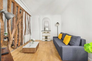 Ein Wohnzimmer mit grauem Sofa, Holzboden, Couchtisch, Spiegel und einer Pflanze.