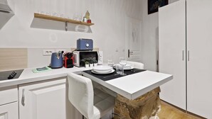 A modern kitchen with white cabinetry, a stone countertop, and a microwave. - Quartier Palais Royal - Studio Apartment NetFlix (Paris)