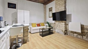 A modern living room with a stone accent wall, a white sofa with colorful cushions, a coffee table, a TV mounted on the wall, and a wooden ceiling. - Quartier Palais Royal - Studio Apartment NetFlix (Paris)