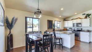 A modern kitchen with white cabinets, a central island, and a dining area with wooden chairs and a table. - Desert Escape w/ Spool Pool! 4 Mi to Lake Havasu (Lake Havasu City)