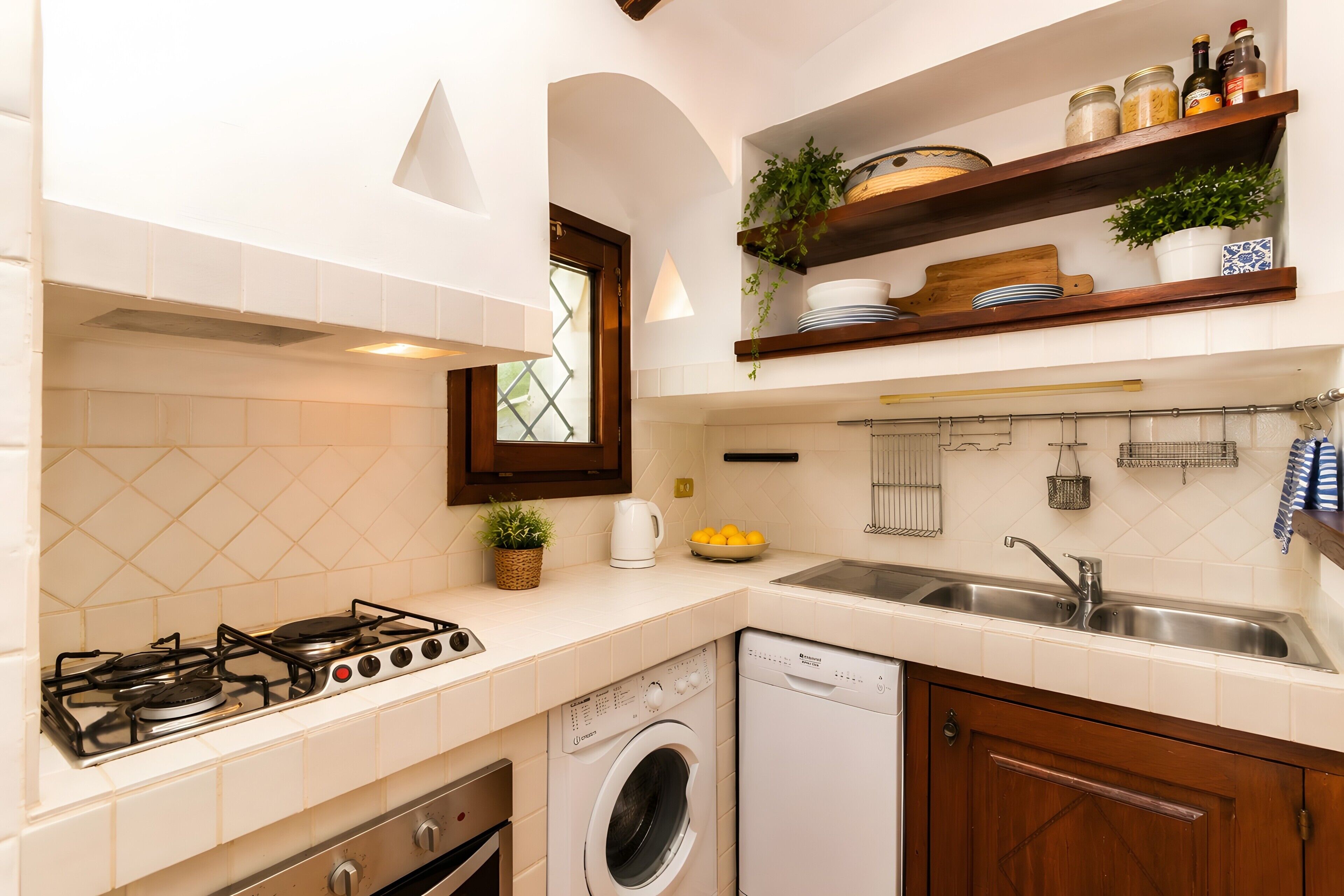 Une cuisine compacte équipée d’une cuisinière à gaz, d’un lave-linge, d’un évier et d’une petite fenêtre.