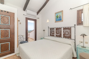 A bedroom with a bed, a painting, a window with curtains, and a door. - Apartment 'Casa Ilaria' with Shared Pool, Private Terrace, and Wi-Fi (Liscia di Vacca)