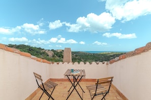 Una terraza con una mesa y sillas, con vista a un paisaje pintoresco lleno de vegetación y una lejana vista al mar.