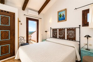 Une chambre à coucher avec un lit, une porte en bois ornée de motifs géométriques, un tableau et une vue sur l’extérieur.