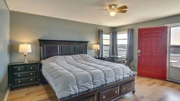 A bedroom with a bed, nightstands, a desk, a red door, and a ceiling fan.