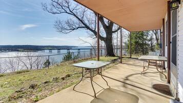 A covered patio with a table and chair, overlooking a body of water with a bridge in the distance.