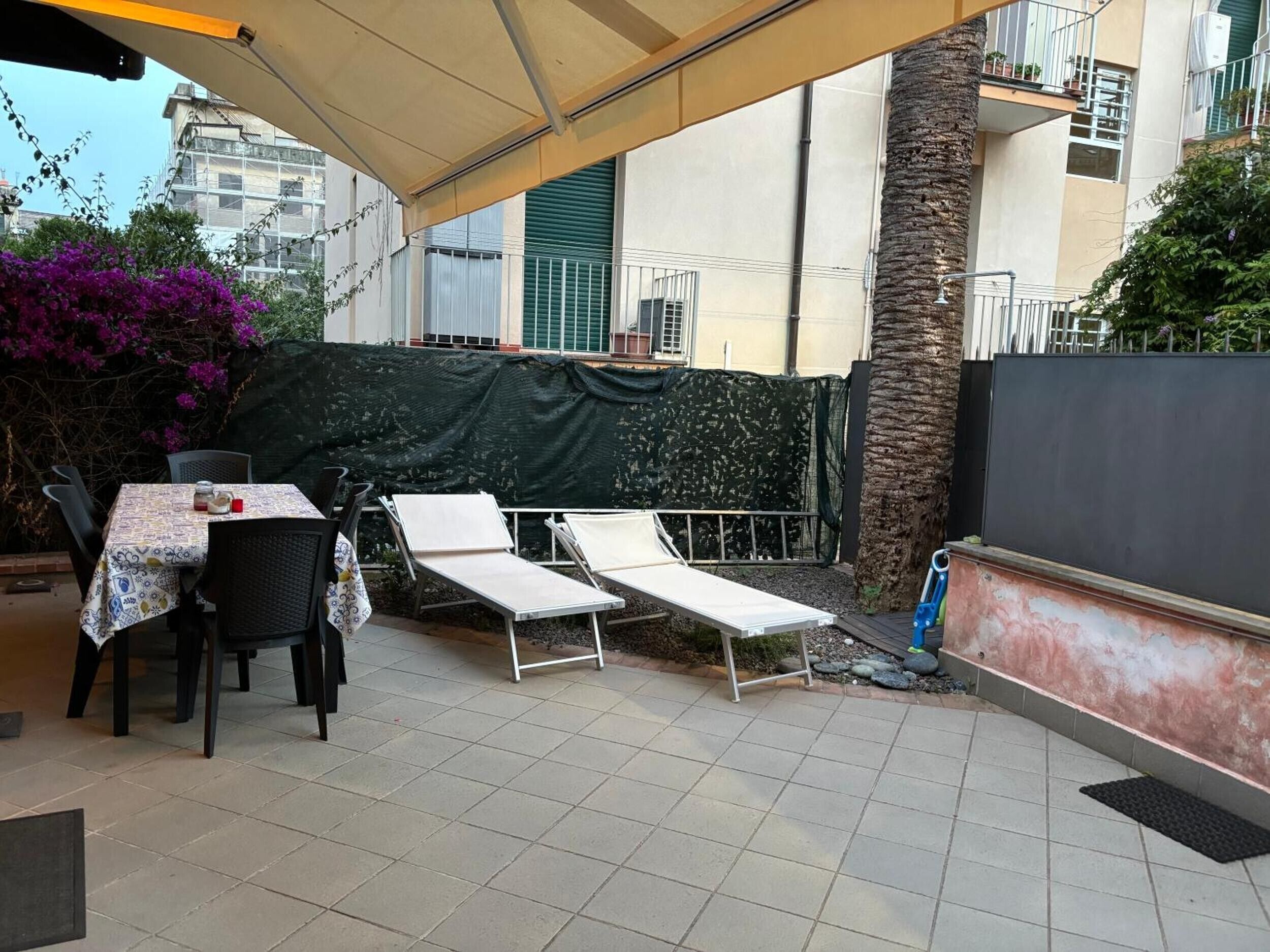 Un patio al aire libre con una mesa y sillas, un área de descanso cubierta y vistas a un edificio con balcones.