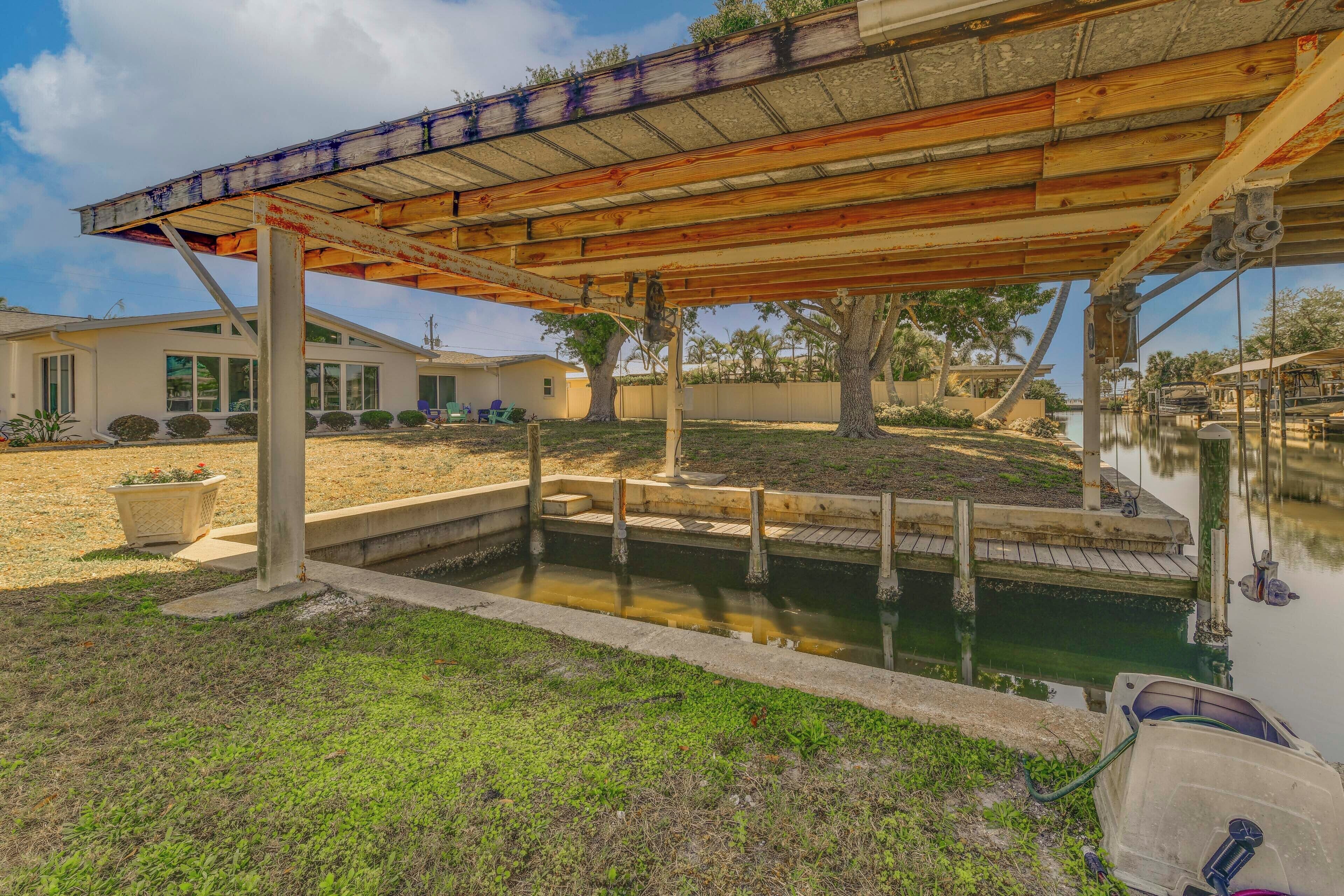 A covered outdoor area with a concrete pool, wooden deck, and a house in the background.