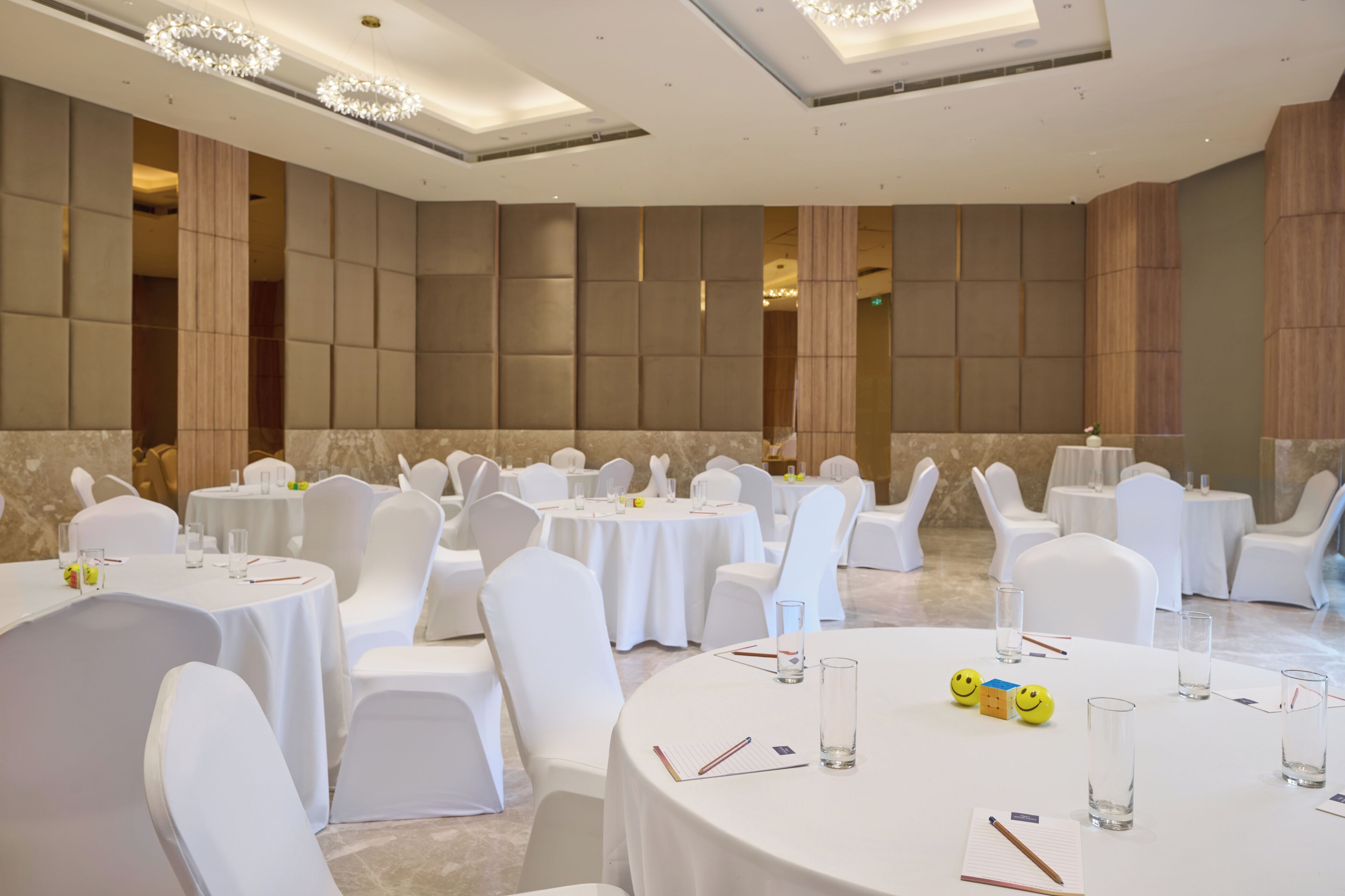 Une salle de conférence avec des tables rondes, des chaises blanches et un lustre.