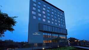 A modern multi-story hotel with a flat facade, large windows, and a visible entrance with a gated driveway.