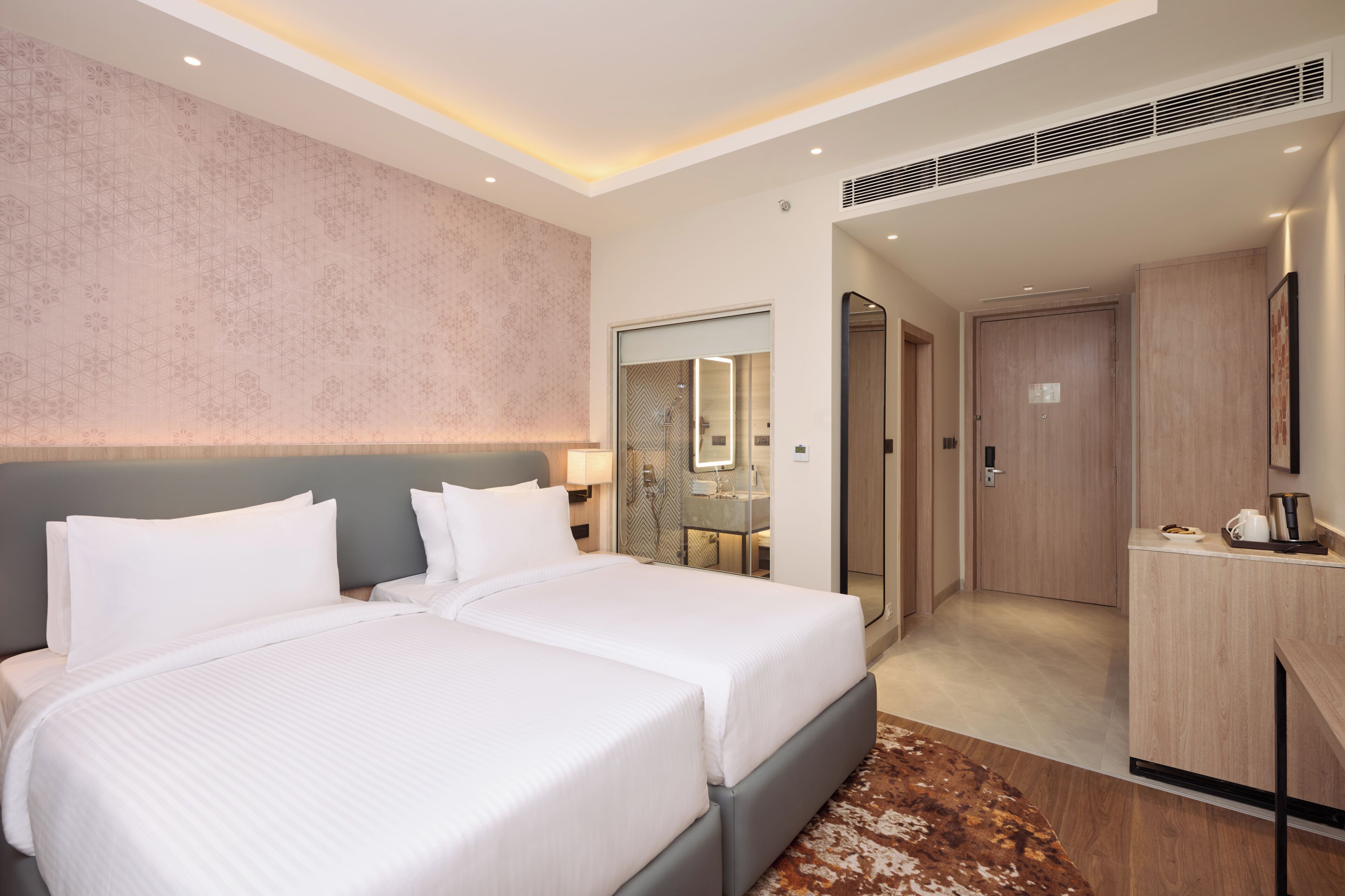 A hotel room with two beds, a walk-in closet, and a bathroom with a shower and mirror.