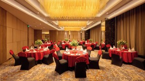 A banquet hall with round tables, black chairs, and red tablecloths.
