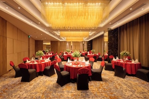 A banquet hall with round tables, black chairs, and red tablecloths. - KPG Sarovar Portico, Rajnagar Extension, Ghaziabad (Ghaziabad)