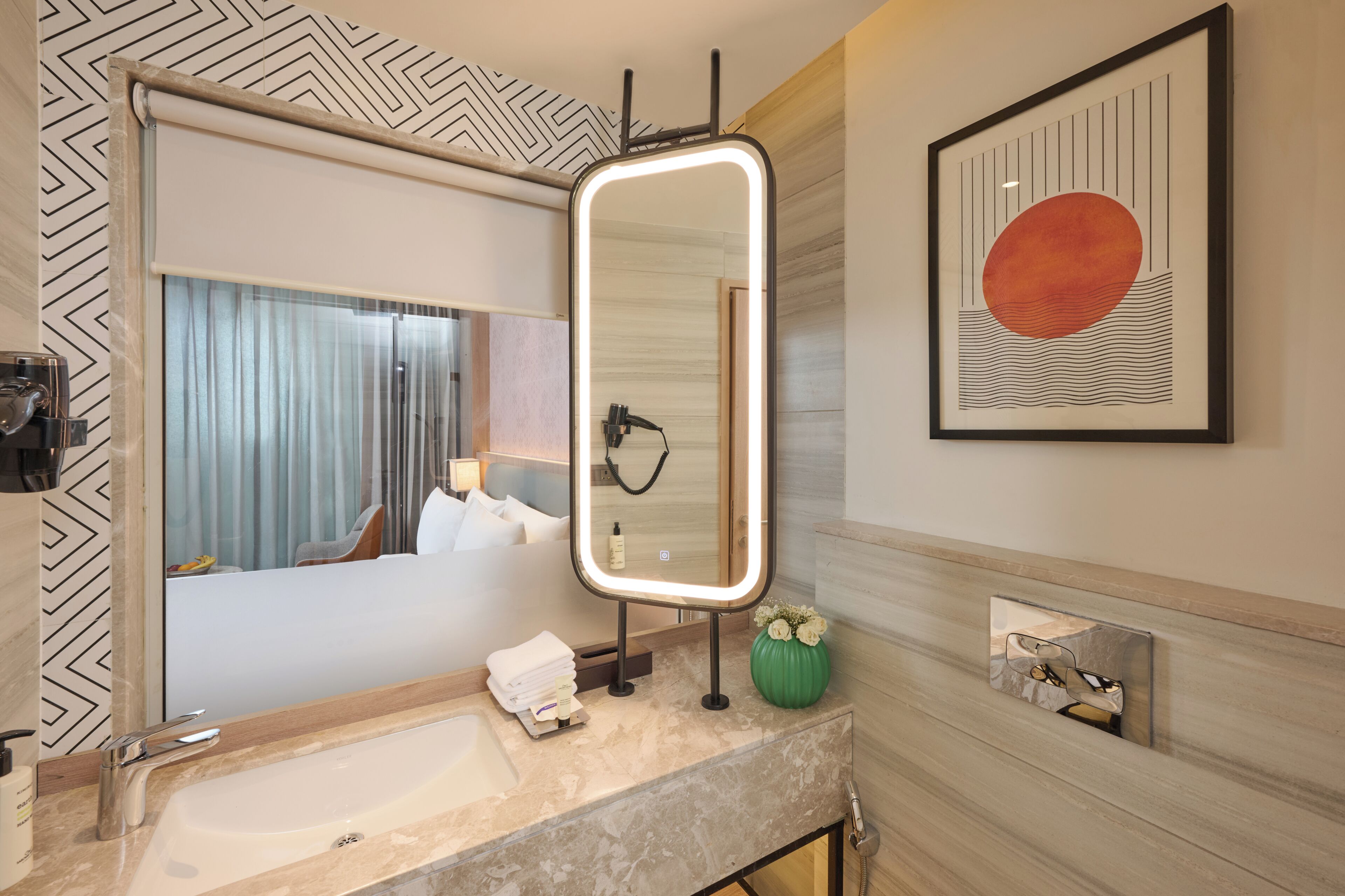 Un bany modern amb un mirall gran, un lavabo, un assecador i una obra d'art penjada a la paret.
