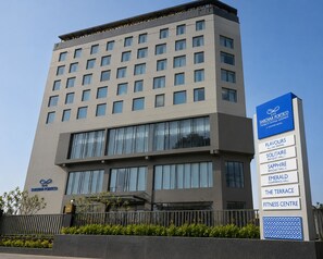Edifici modern d'hotel amb diverses plantes, grans finestres i una placa informativa que detalla serveis com ara restauració, sales de banquet i centre de fitness.