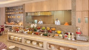 A buffet area with various food stations, a kitchen in the background, and a seating area with tables and chairs.