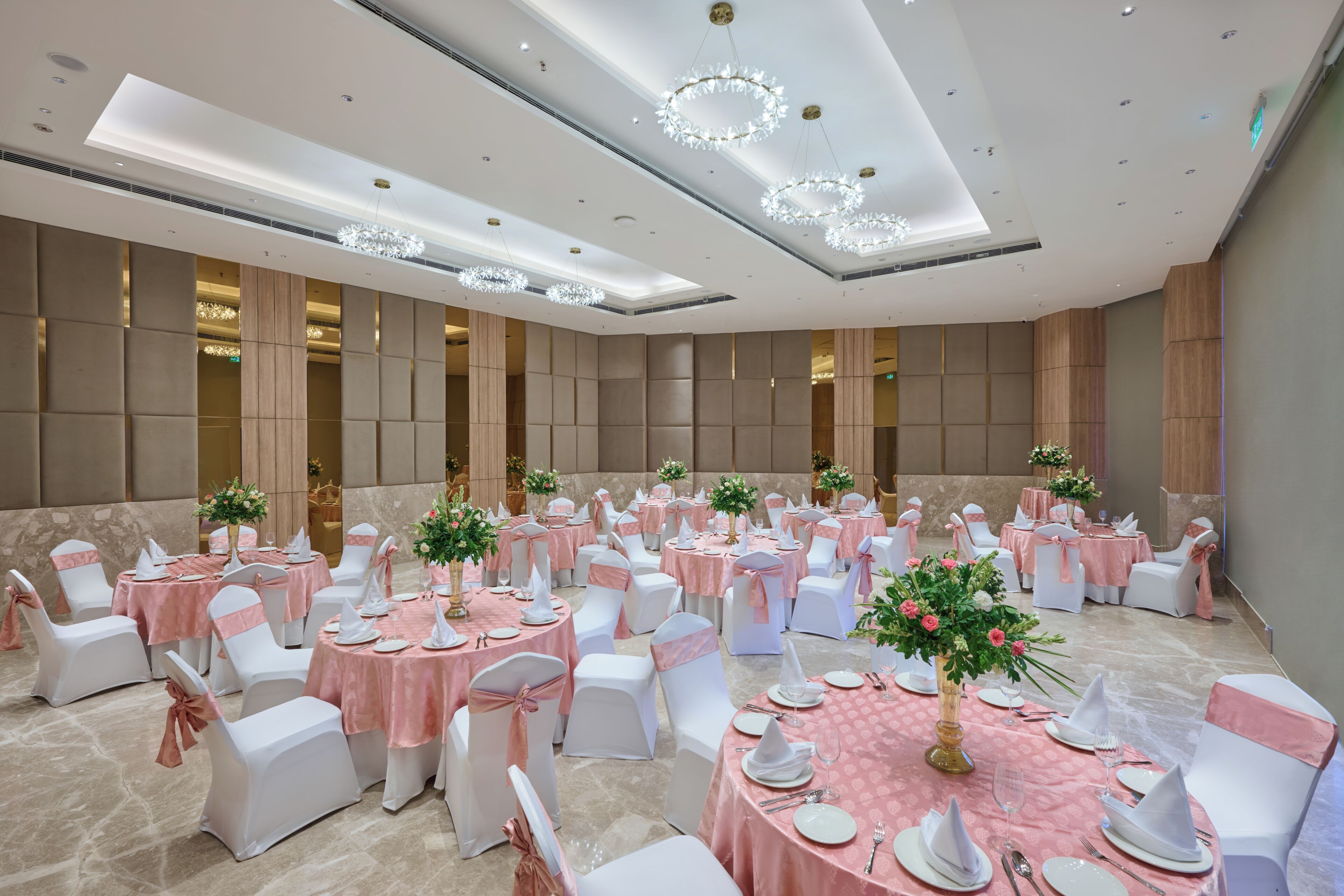 Un salón de banquetes con mesas redondas, sillas blancas y manteles rosas.