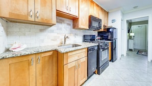 A kitchen with wooden cabinets, granite countertop, stainless steel appliances, and a tiled backsplash. - Steps to Beach! Pompano Beach Apt w/ Shared Pool (Pompano Beach)