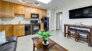 A modern kitchen with wooden cabinets, a microwave, stove, and a large TV. - Steps to Beach! Pompano Beach Apt w/ Shared Pool (Pompano Beach)