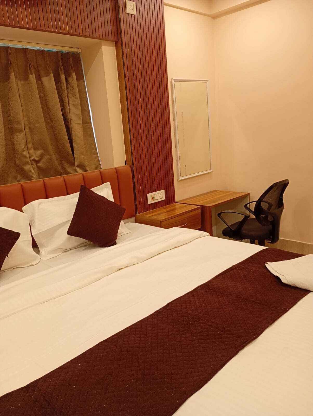 A hotel room with a bed, a desk, a chair, a mirror, and a window with curtains.