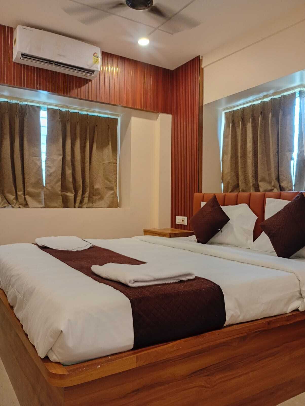 Habitación de hotel con una cama de madera, dos ventanas con cortinas, un equipo de aire acondicionado y un ventilador de techo.