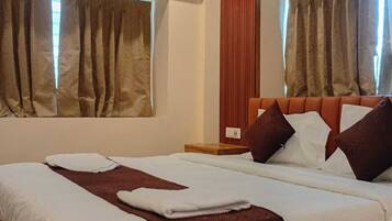 Habitación de hotel con una cama de madera, dos ventanas con cortinas, un equipo de aire acondicionado y un ventilador de techo.