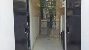 A glass door entrance with a push bar, leading to a corridor with a person walking inside. - The Executive Suites (Barasat)