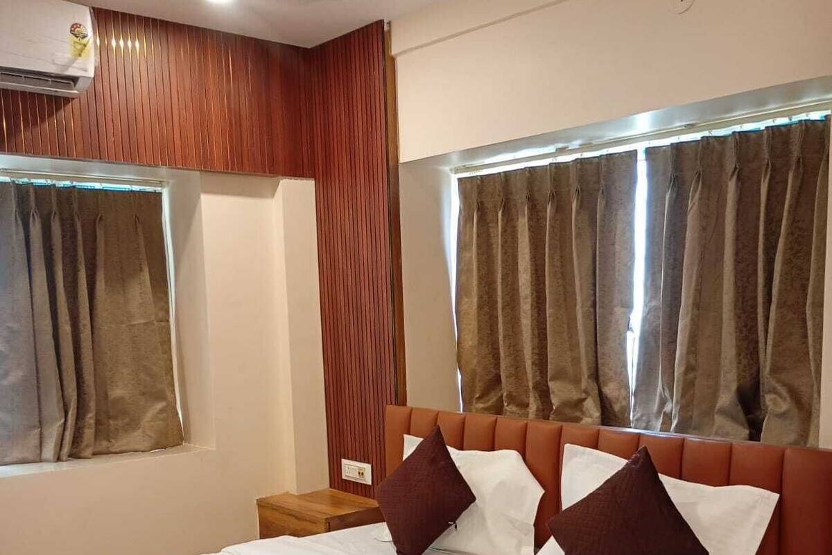 A hotel room with a large bed, wooden headboard, two bedside tables, and a window with curtains.