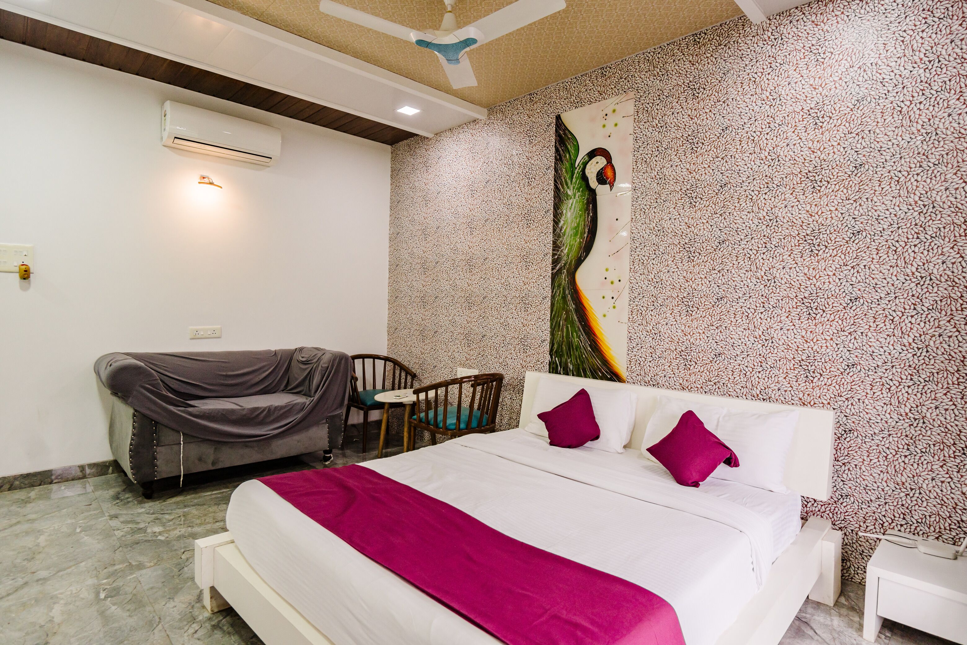 A hotel room with a bed, a chair, a small table, an air conditioning unit, and a wall with a textured pattern.