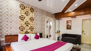 Quarto de hotel com uma cama grande, cabeceira de madeira, um sofá e uma parede com padrão.