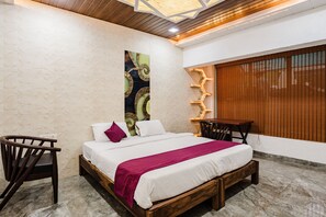A bedroom with a bed, a wooden chair, a small table, and a window with blinds. - Alaya Stays Moonstone meadows With Pool (Lonavala)