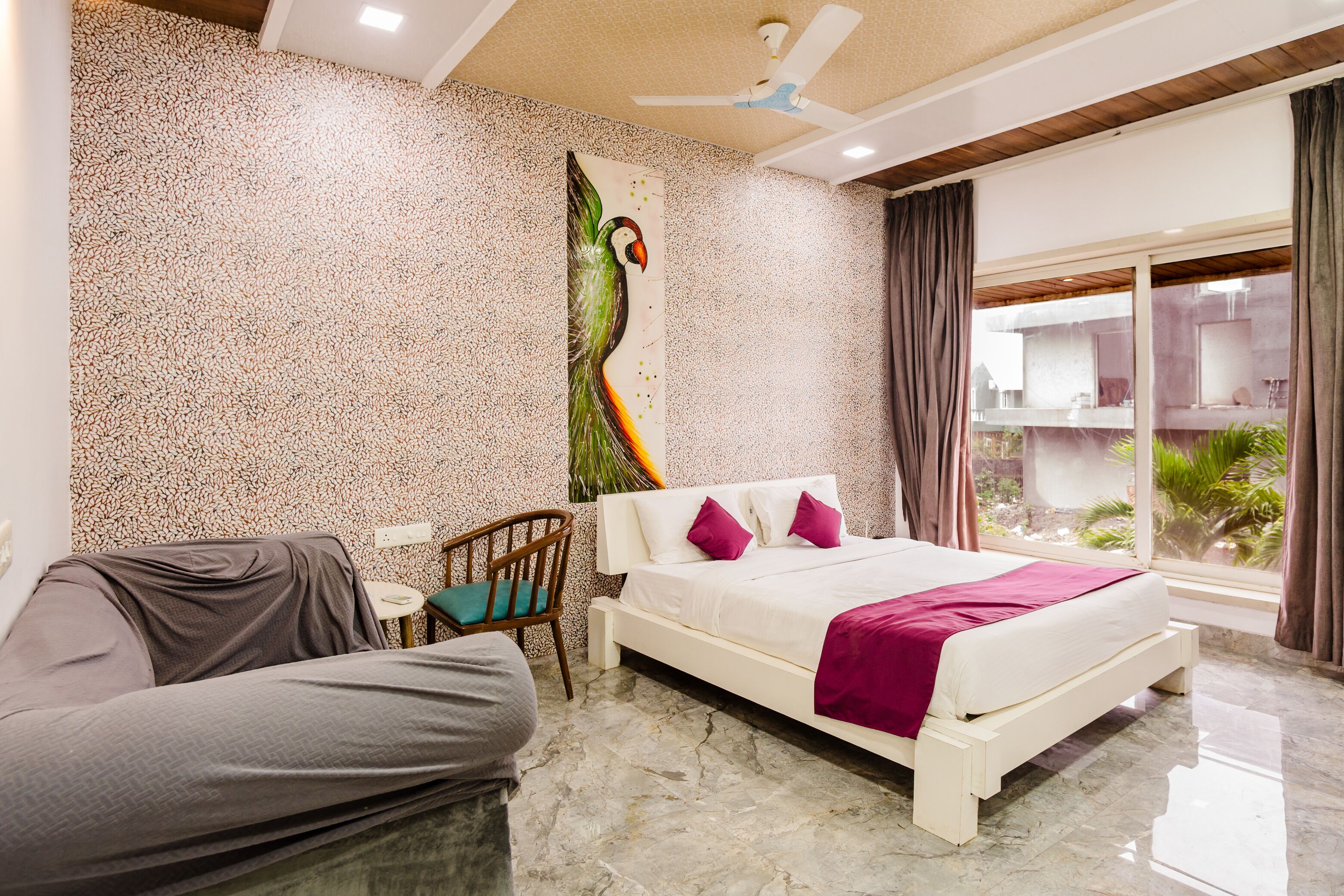 Une chambre à coucher comprenant un lit, une chaise, une petite table, un ventilateur de plafond et une vue sur l’extérieur.