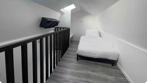Ein schmaler Korridor mit Oberlicht, einem Bett und einem an der Wand befestigten Fernseher.