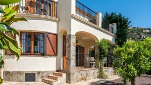 A two-story building with stone arches, a balcony with a railing, and a staircase leading to the entrance. - Casa Baringo, pool and sea view (Calonge)