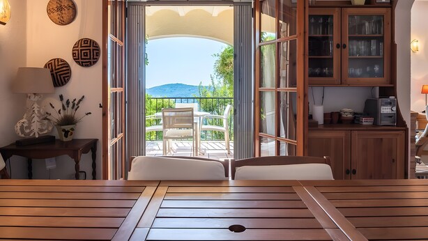A wooden table with chairs, a view of the outdoors, a cabinet with glass doors, and decorative wall art. - Casa Baringo, pool and sea view (Calonge)