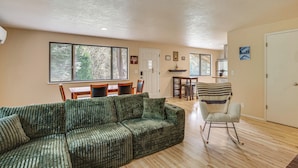 A living room with a sectional sofa, a rocking chair, a dining area with a table and chairs, and a kitchen area with a refrigerator and a sink. - Creative Escape! Eagle's Nest Hideaway (Cottage Grove)