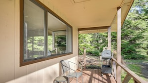 A covered porch with a view of a wooded area, a grill, and a chair. - Creative Escape! Eagle's Nest Hideaway (Cottage Grove)
