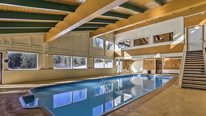 Ein Innenpool mit Holzbalkendecke, großen Fenstern und einer Treppe, die zu einer oberen Ebene führt.