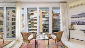 A balcony with a view of a high-rise building, wicker chairs, a glass table, and a patterned rug. - Solaga - Maestranza (Málaga)