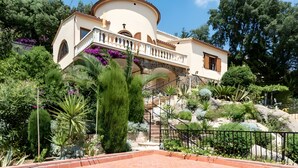 Een villa in mediterrane stijl met een stenen trap, een weelderige tuin en een terras.
