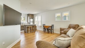 A living room with a brown sofa, a dining area with a wooden table and chairs, and a kitchen with a refrigerator and a sink. - Walk to Dtwn: Rochester Home, Private Deck + Yard! (Rochester)