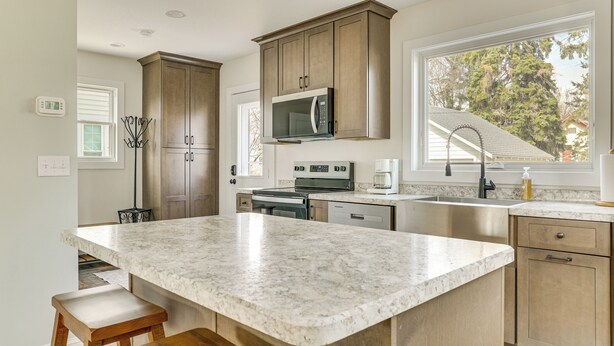 A kitchen with a large island, wooden cabinets, stainless steel appliances, and a window with a view of trees. - Walk to Dtwn: Rochester Home, Private Deck + Yard! (Rochester)