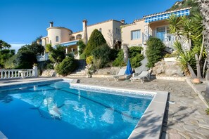 Una piscina con agua cristalina, un deck de piedra y un edificio con toldo azul.