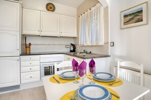 Une cuisine avec des meubles blancs, un évier et une table à manger dressée avec des assiettes et des serviettes.