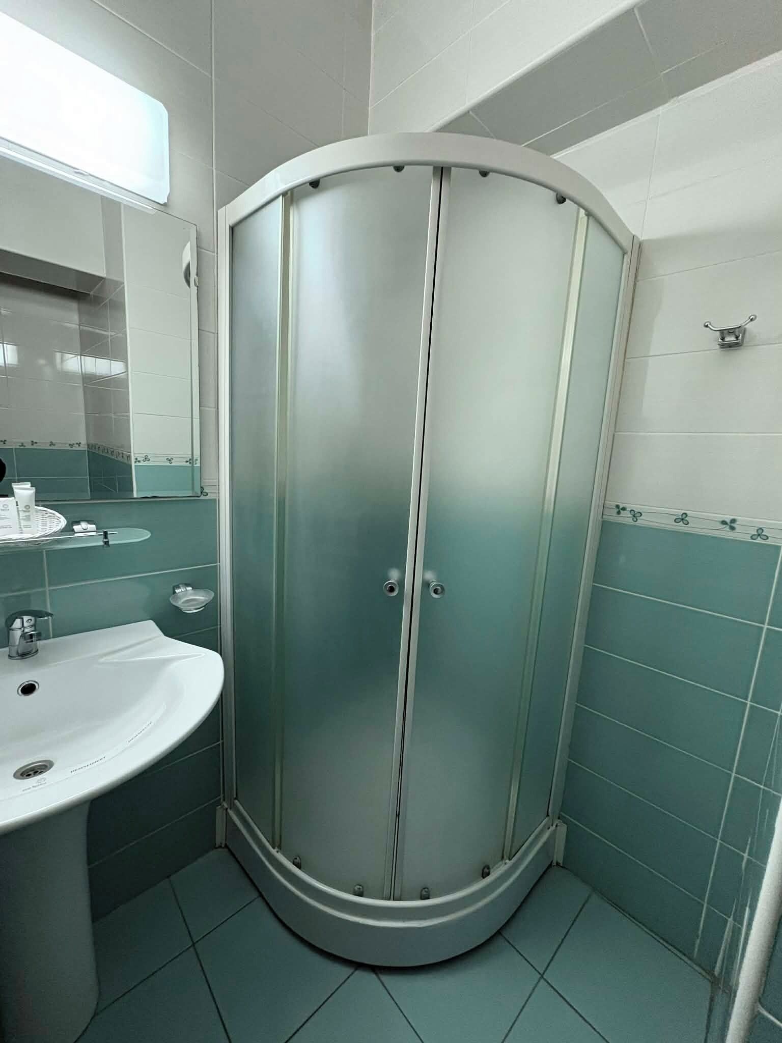 Un baño con cabina de ducha curva, lavamanos y espejo.