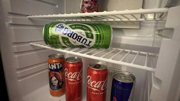 A refrigerator with a bottle of Santa Cruz Fructis, a can of 1880, and several cans of Coca-Cola and Red Bull.