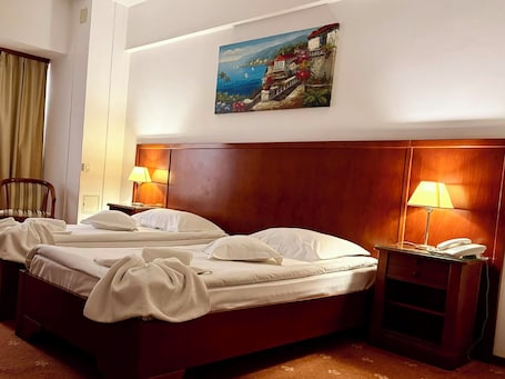 Habitación de hotel con cabecera de madera, dos camas, un cuadro con una escena costera y dos lámparas de noche.